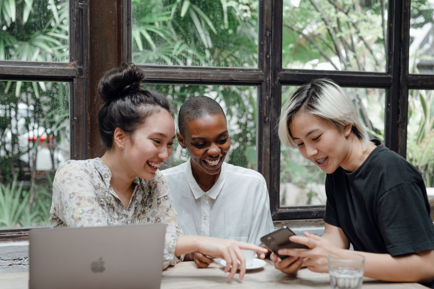 Women entrepreneurs laughing together over a laptop in a cafe